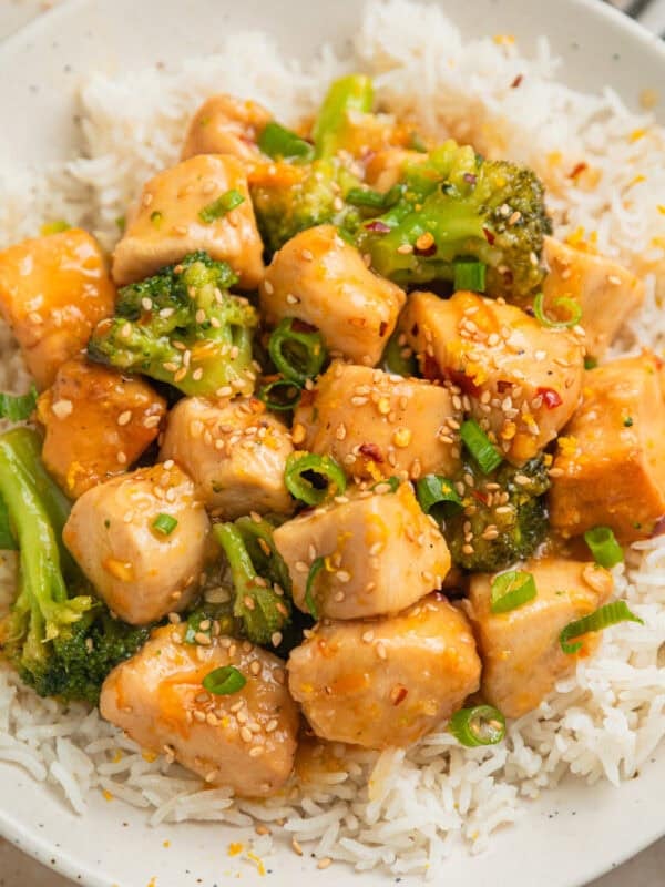 Orange chicken with broccoli served over rice and topped with sesame seeds.