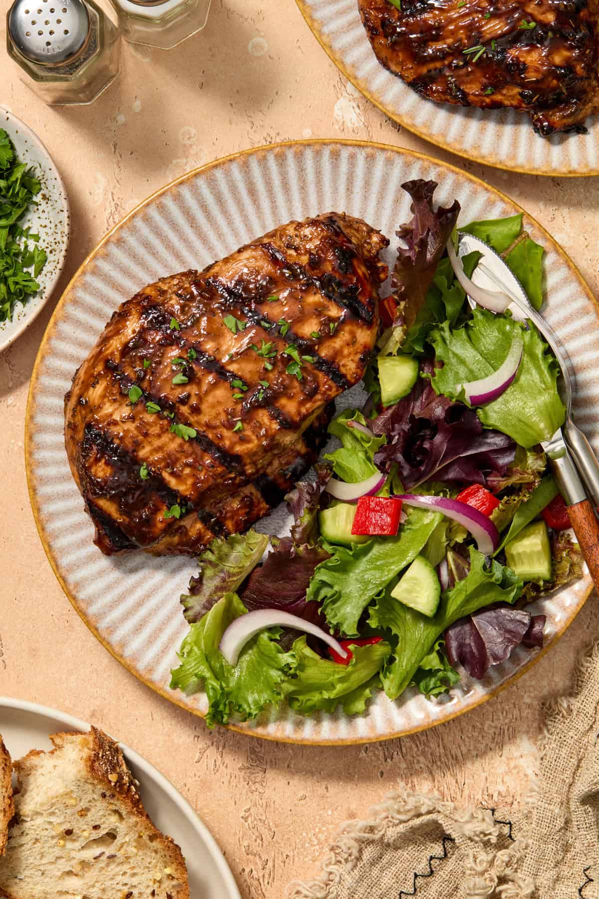Balsamic grilled chicken on plate with salad and chopped parsley over top.
