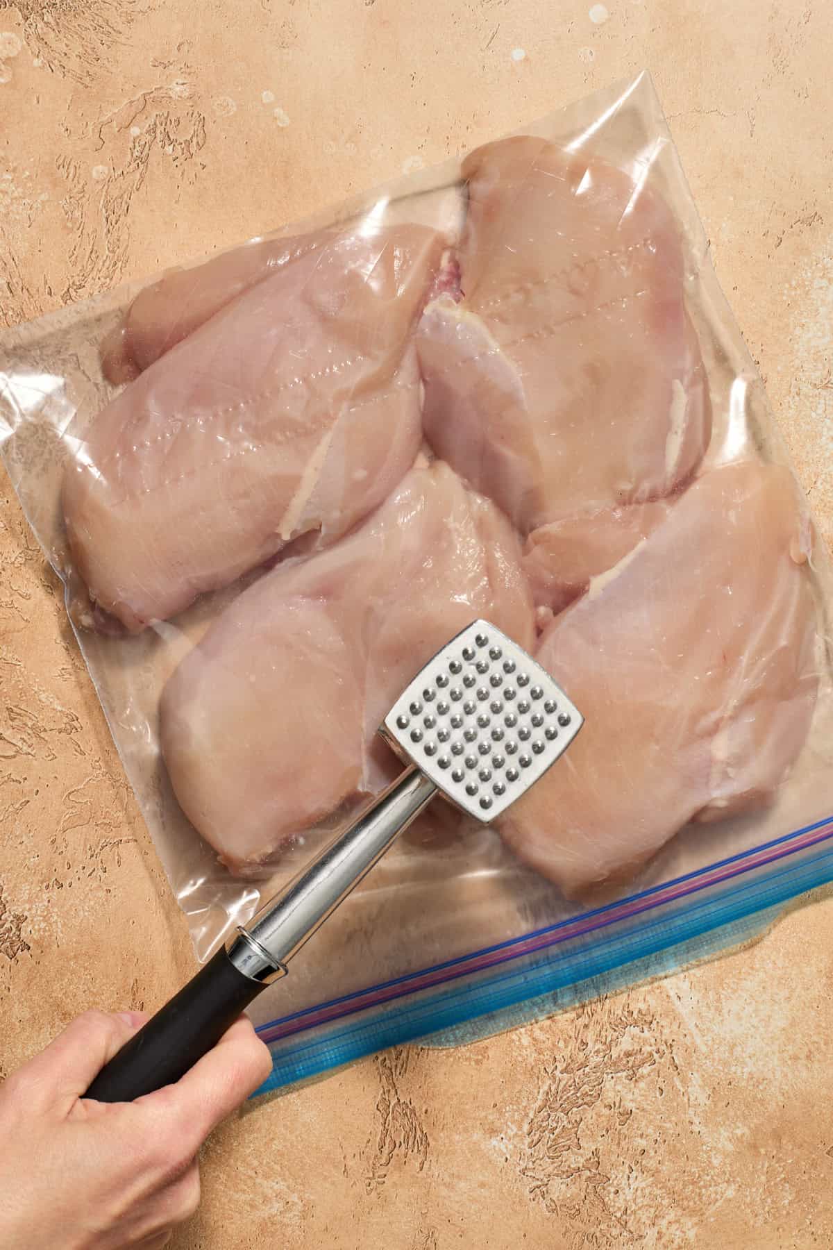Chicken breast in plastic bag being pounded with meat tenderizer.
