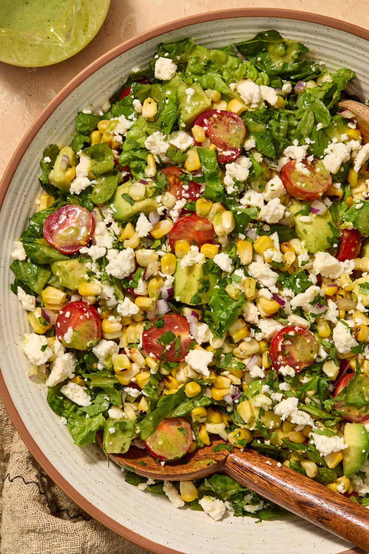 Grilled corn and tomato salad in bowl with wood spoon.
