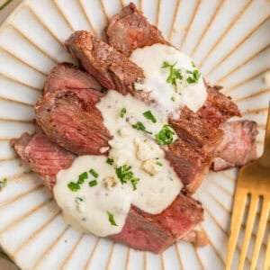 Sliced grilled ribeye steak sliced and served on plate with gorgonzola sauce.