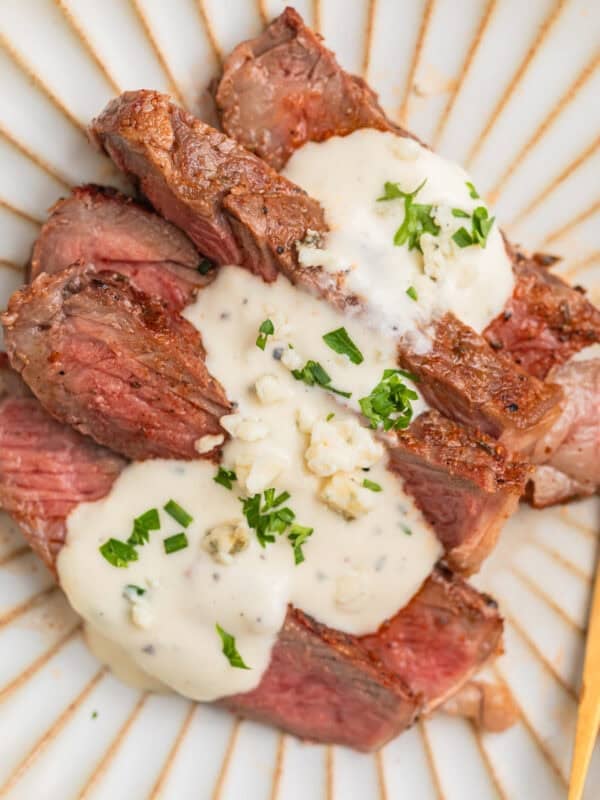 Sliced grilled ribeye steak sliced and served on plate with gorgonzola sauce.