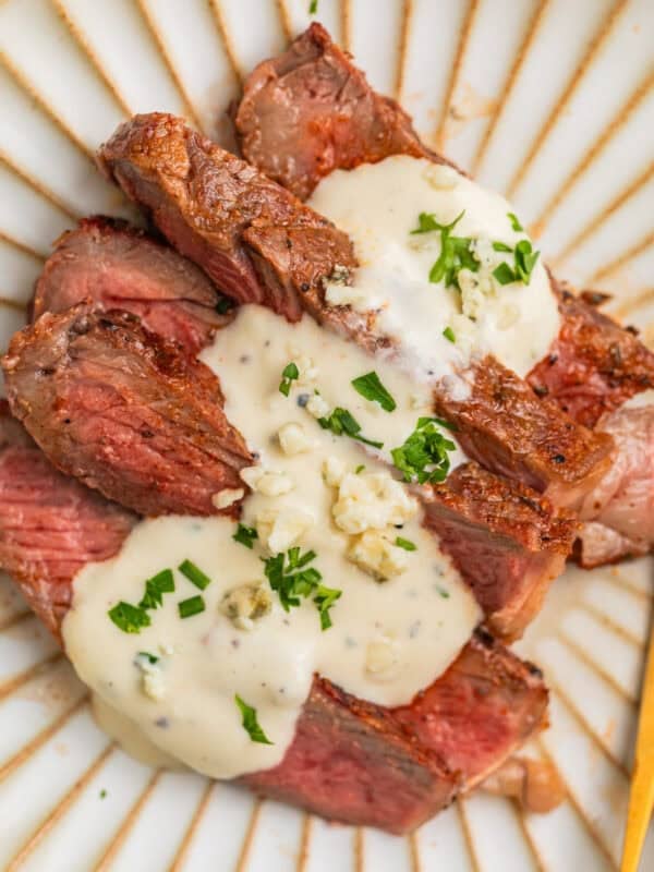 Sliced grilled ribeye steak sliced and served on plate with gorgonzola sauce.