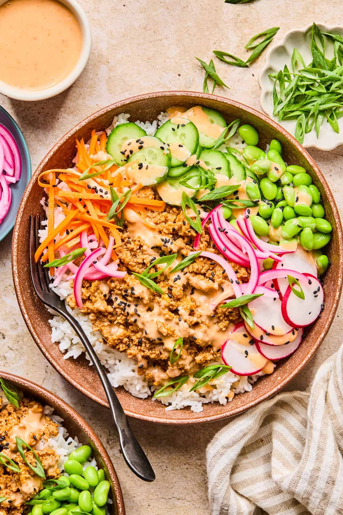 Ground turkey mixture in bowl with rice, mukimame, cucumber and sauce.