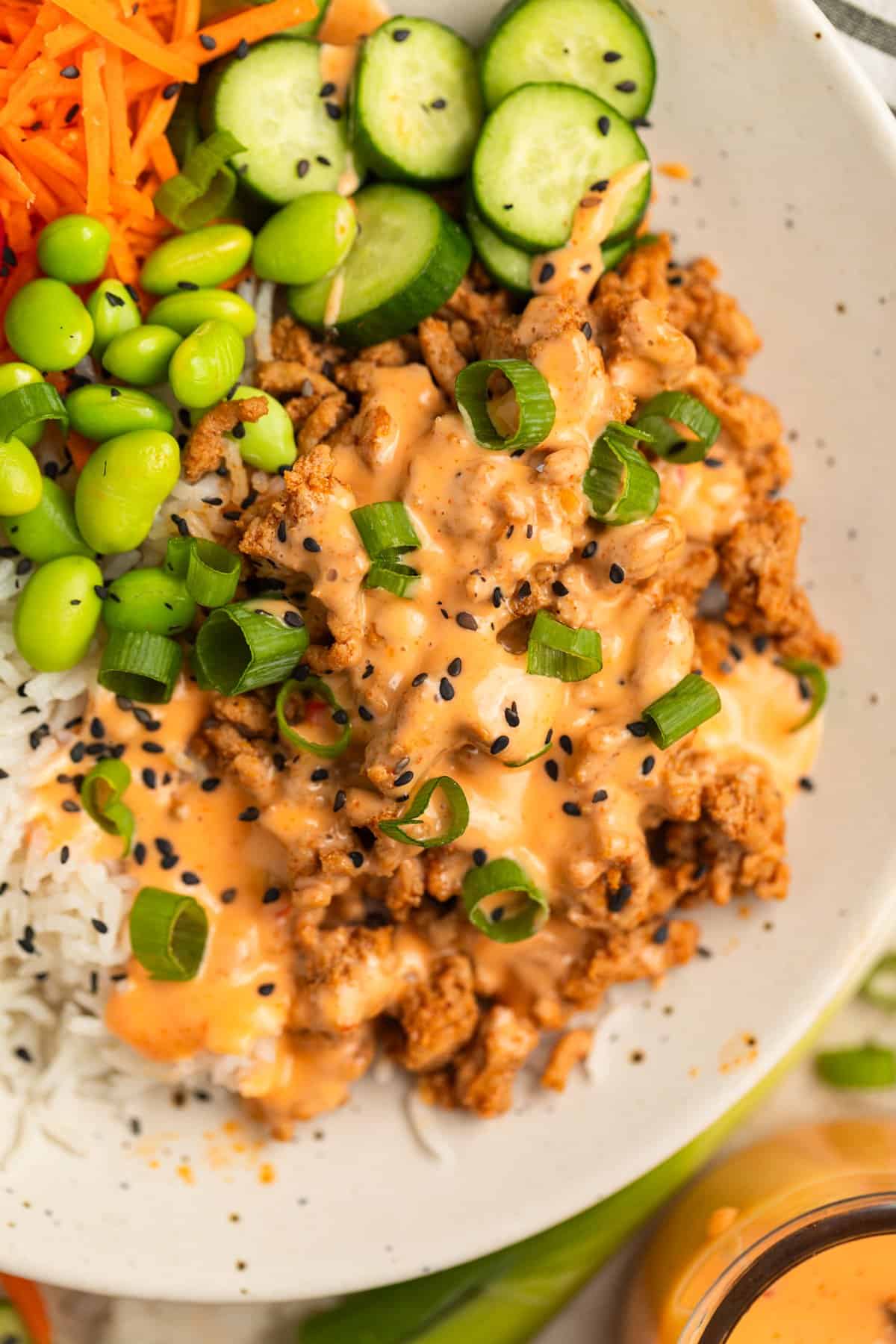 Ground turkey mixture in bowl with rice, mukimame, cucumber and sauce.