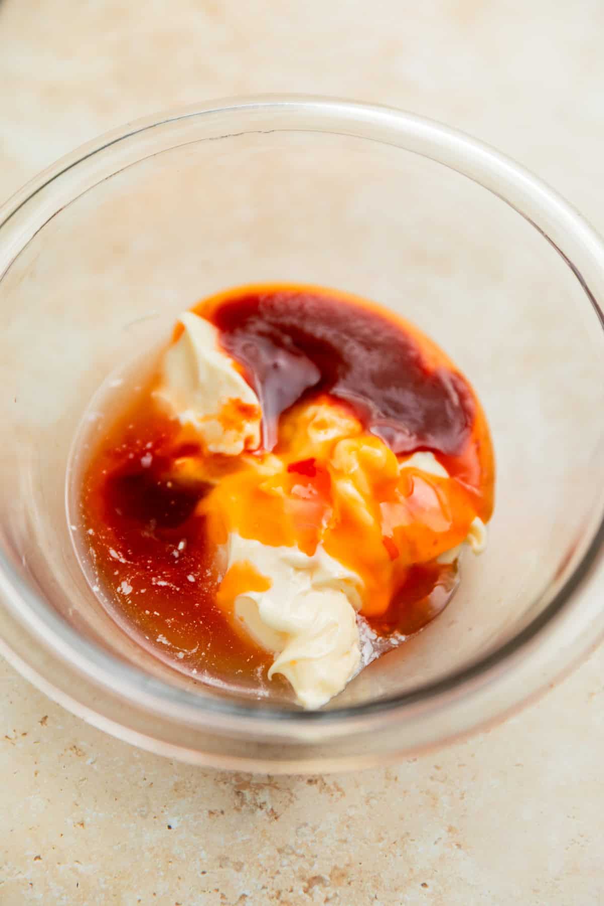 Mayonnaise, sriracha, honey, and ingredients for bang bang sauce in glass dish.