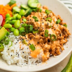 Ground turkey rice bowl with bang bang sauce over top with edamame, cucumber, and more.