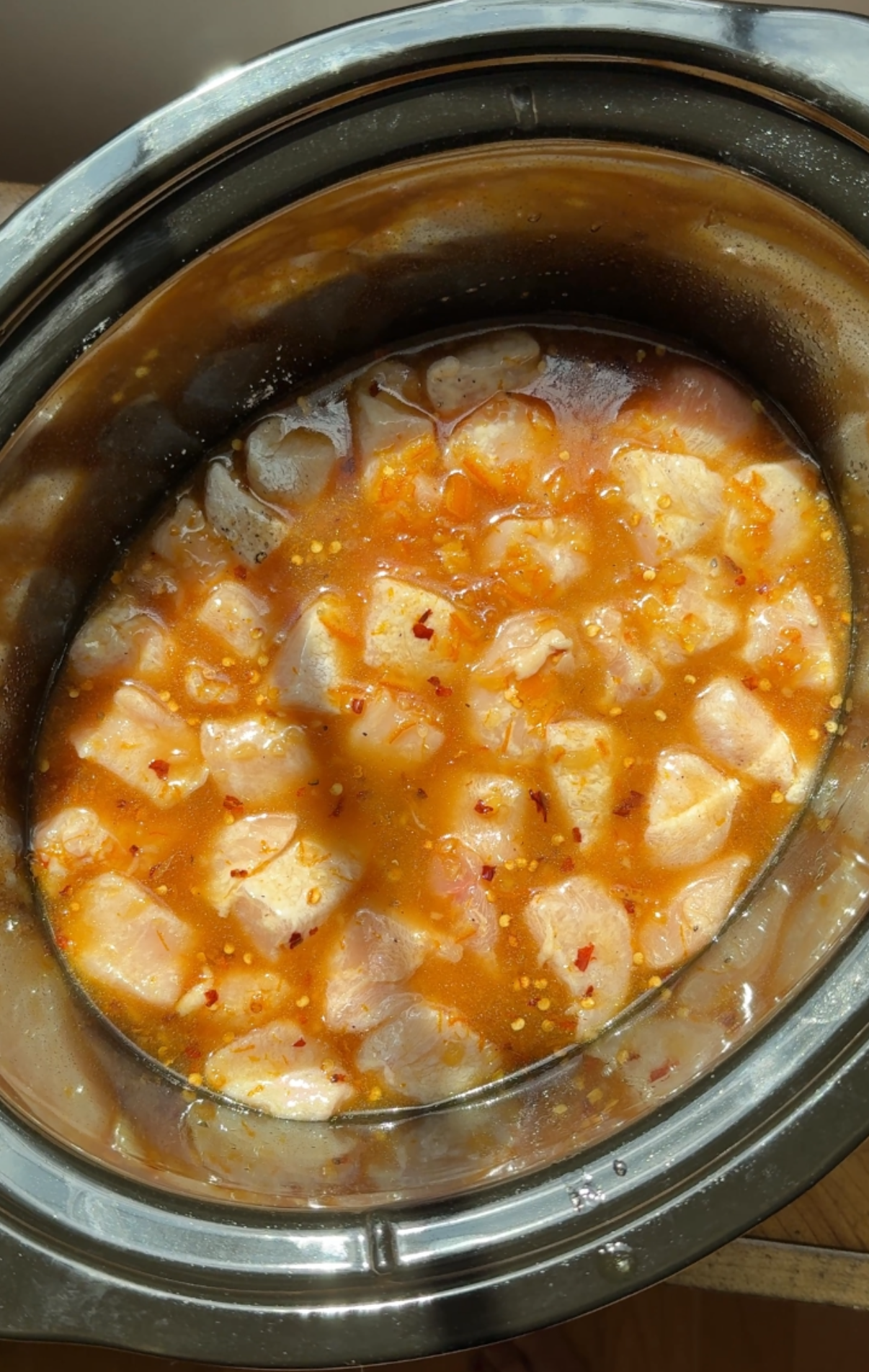 Orange sauce poured over chicken in crock pot.