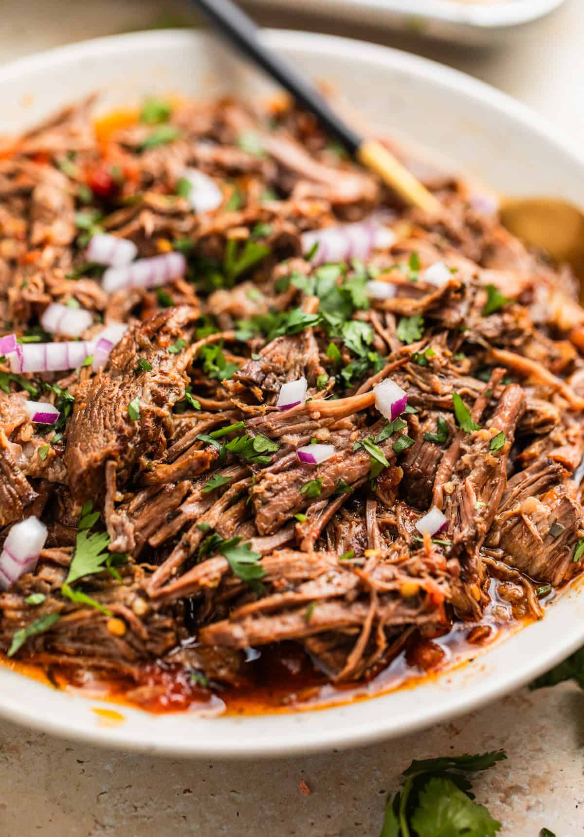 Slow cooker shredded beef tacos in serving plater with spoon.