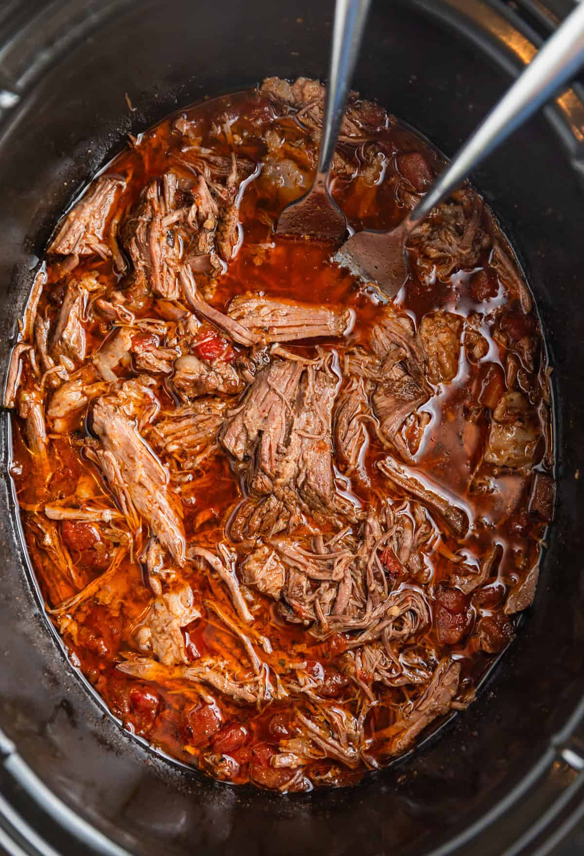 Shredded beef tacos in crock pot with forks.