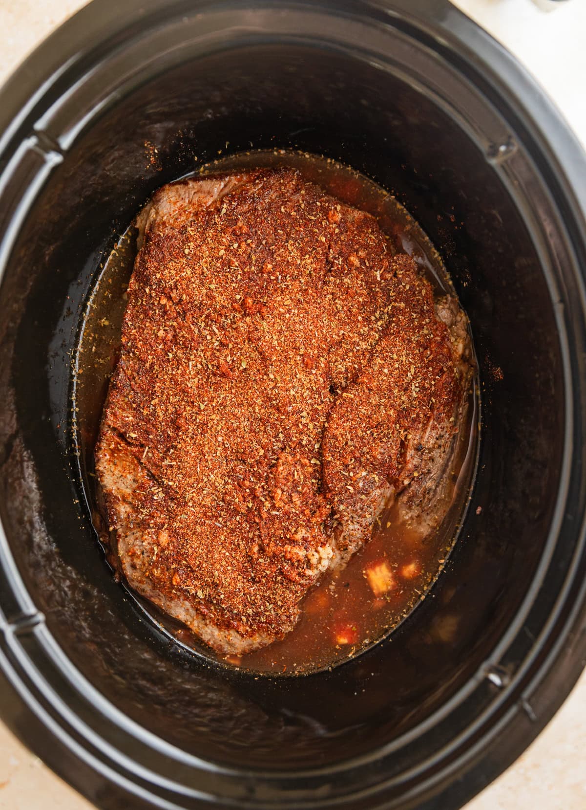 Seasoned beef chuck roast in crock pot before cooking.