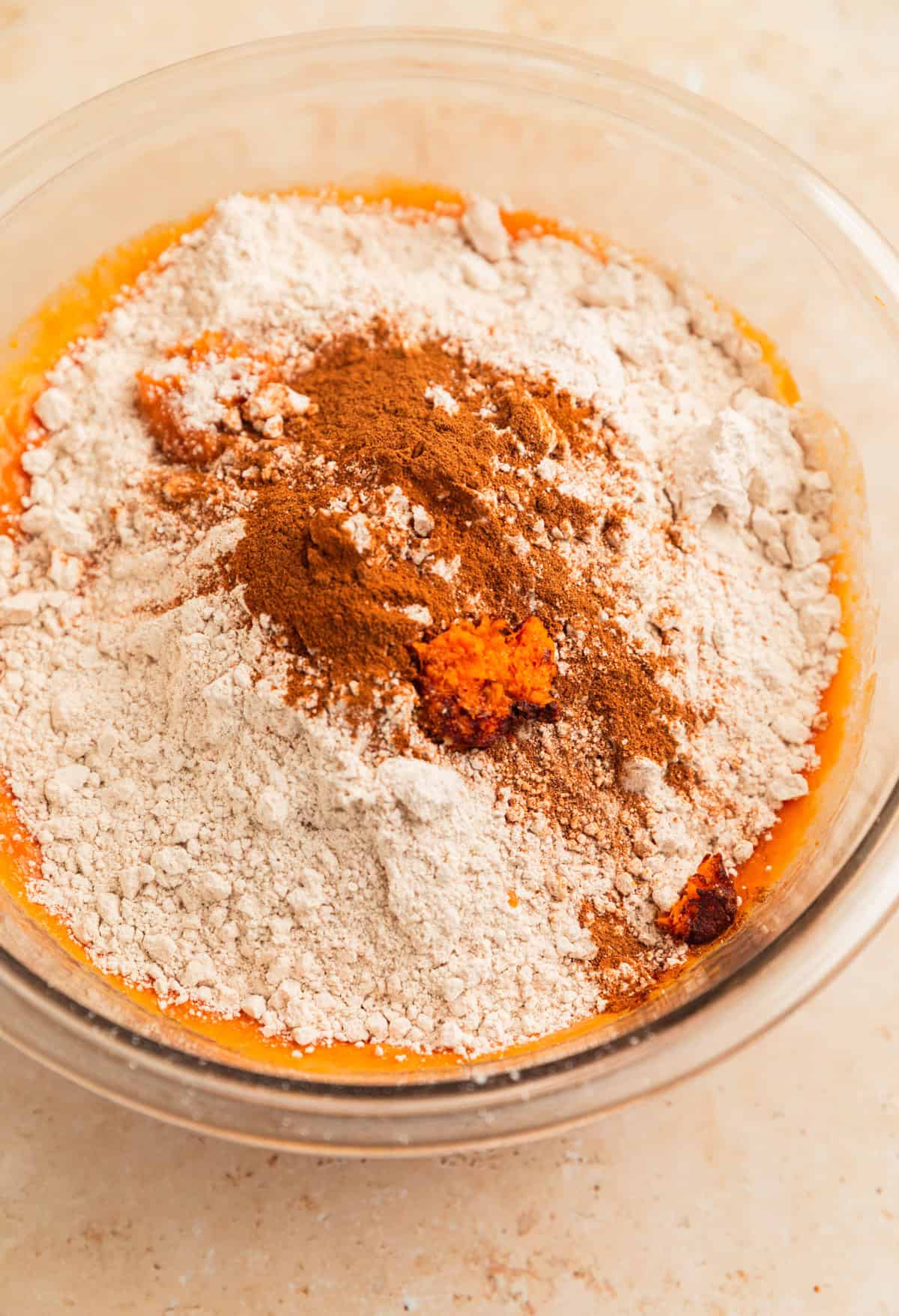 Spice cake mix, pumpkin spice and orange zest added to pumpkin bread wet ingredients in bowl.