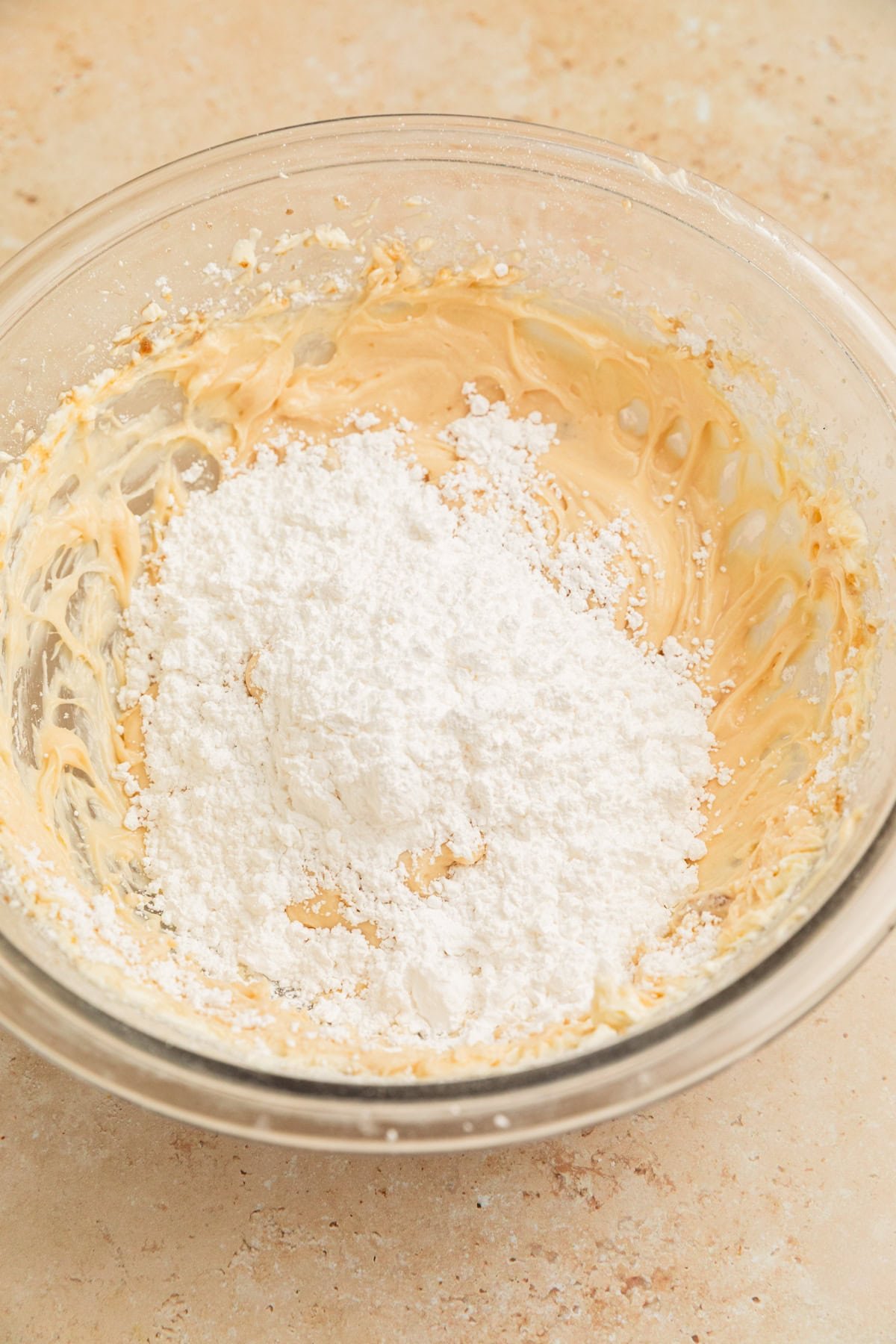 Powdered sugar added to cream cheese frosting mixture in bowl.