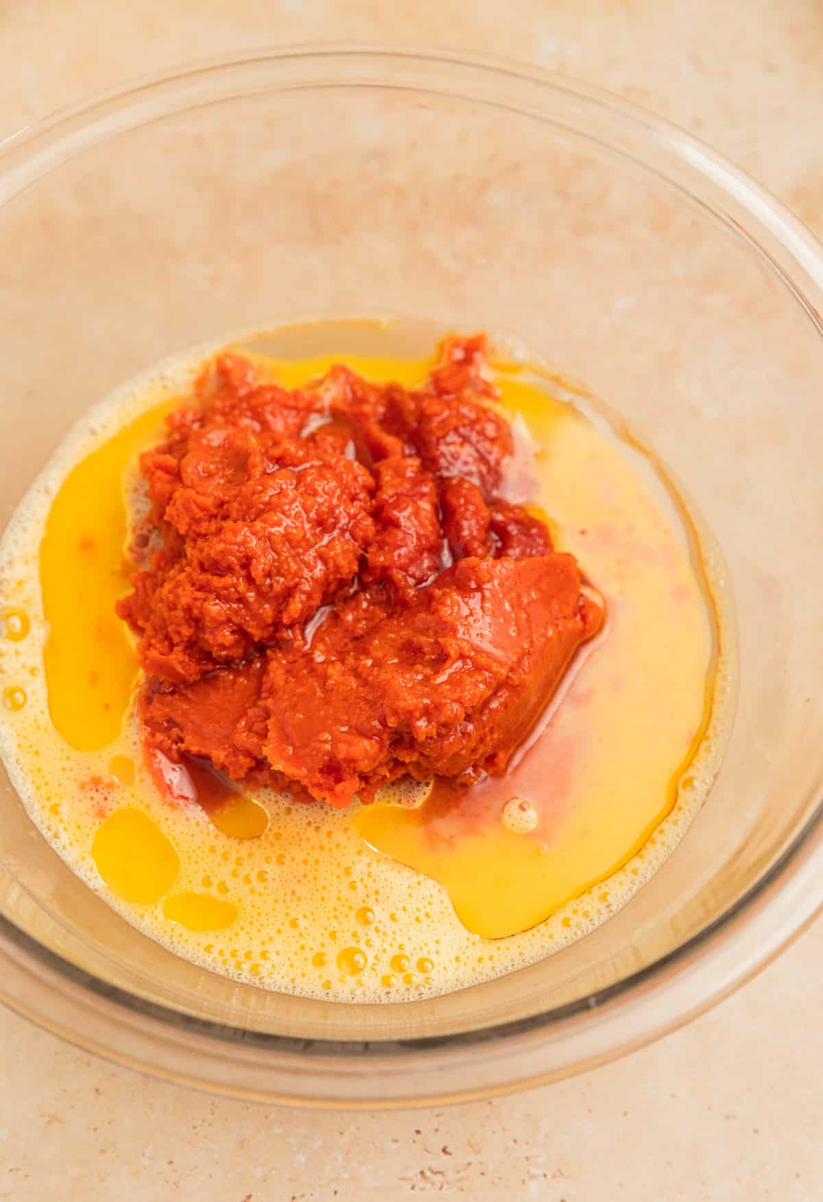 Canned pumpkin, oil, milk and other ingredients added to mixing bowl with eggs.