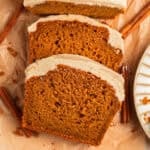 Frosted pumpkin bread slices on parchment with cinnamon sticks.