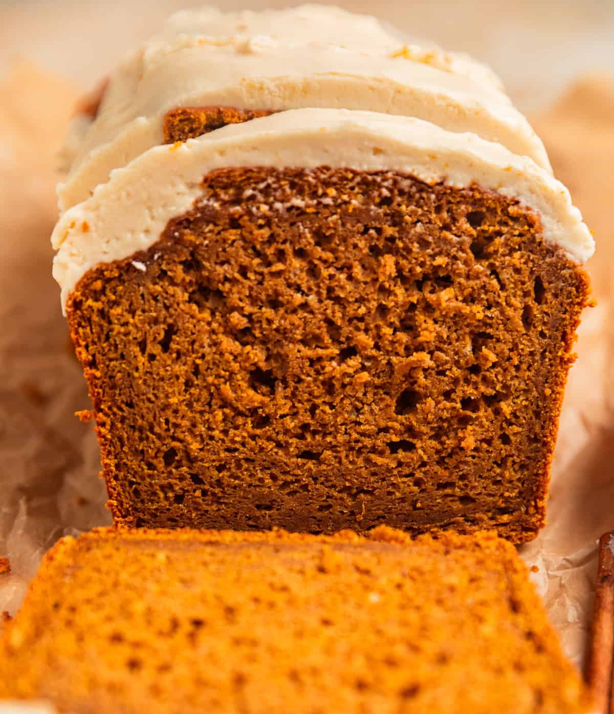 Frosted pumpkin bread loaf with open slice showing texture.
