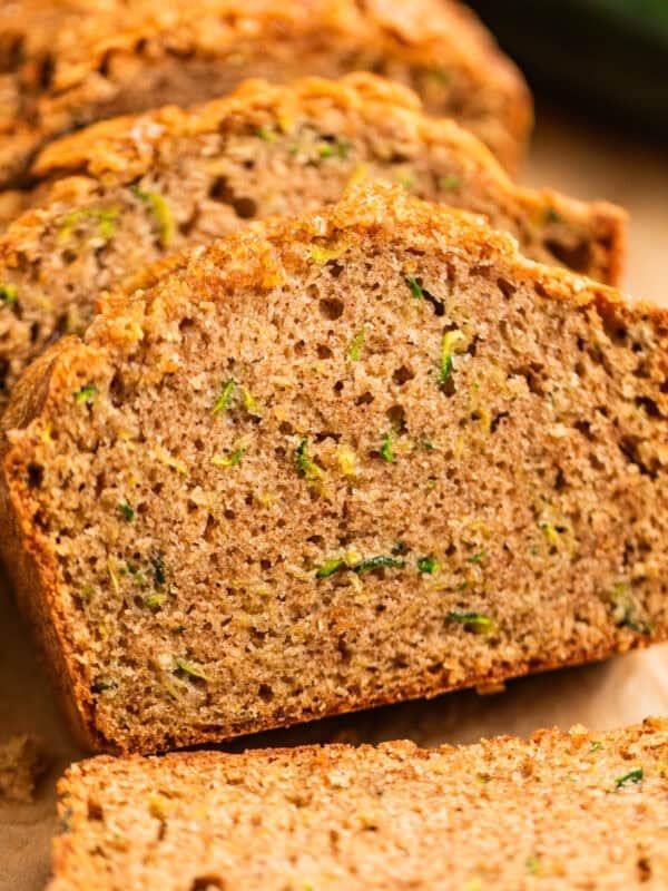 Slices of zucchini bread propped on each other on parchment paper.