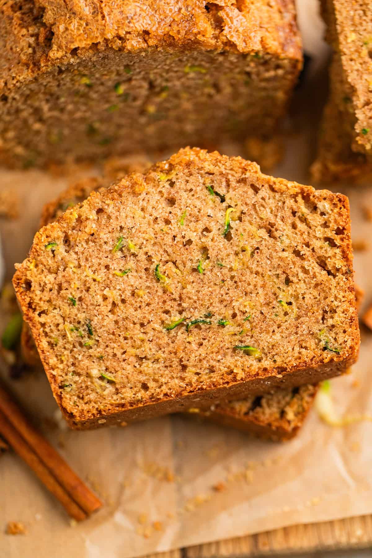 Slices of zucchini bread on parchment with cinnamon sticks beside.