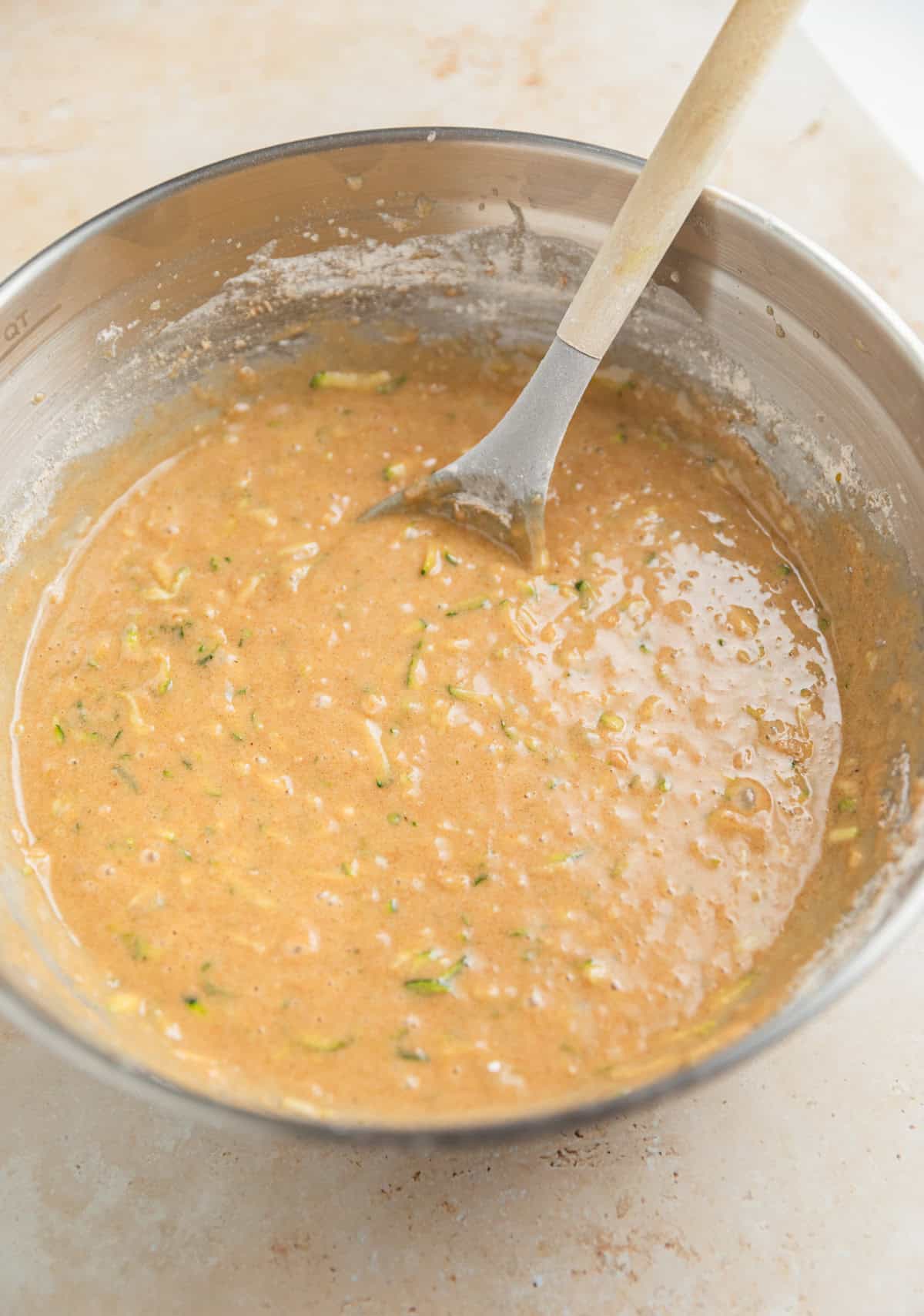 Prepared zucchini bread batter in bowl with wooden spoon.