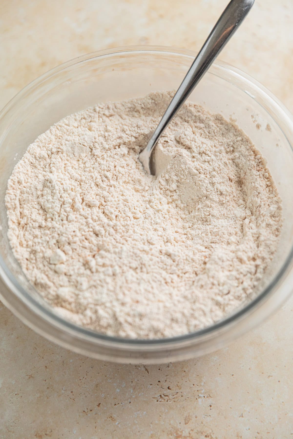 Dry ingredients in glass bowl with spoon. 