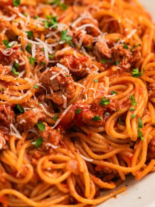 Plate with spaghetti tossed in meat sauce with parmesan and herbs over top.