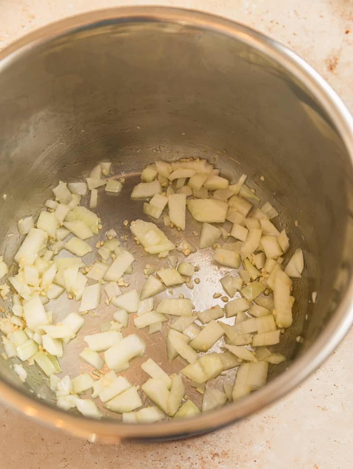 Instant pot with onions being sautéed.