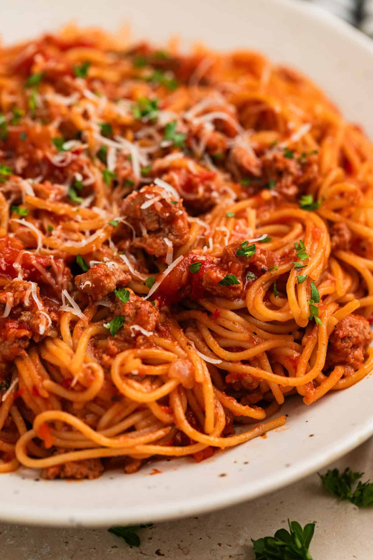 Plate with spaghetti and meat sauce topped with chopped parsley and freshly grated parmesan.