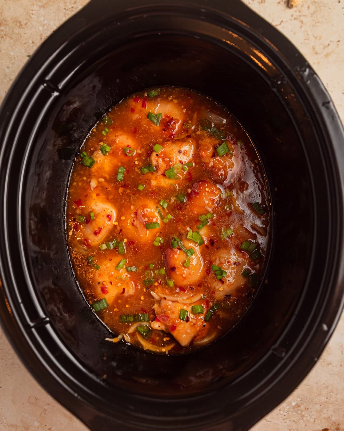 Slow cooker apricot chicken in pot topped with sliced green onions on top.