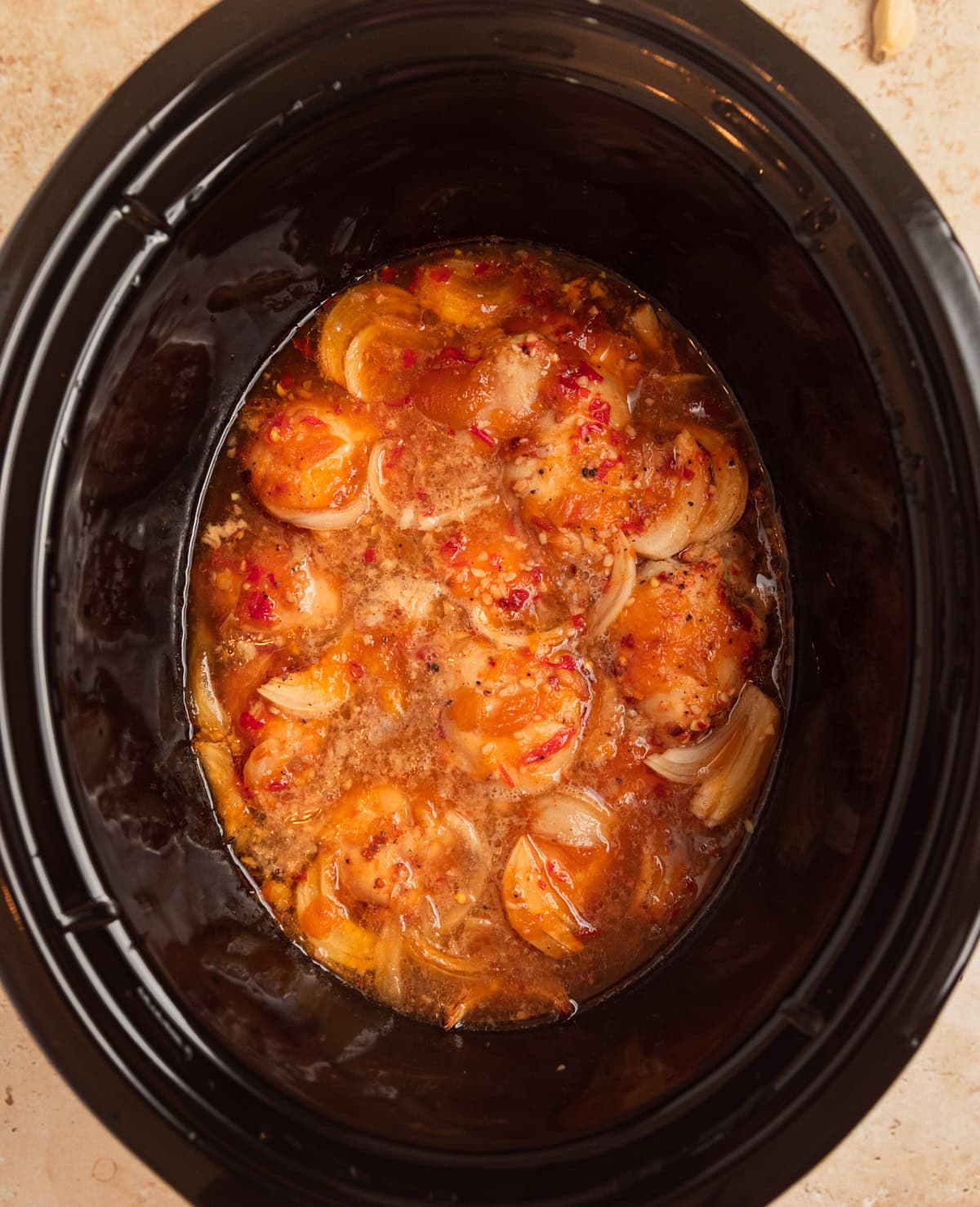 Cooked chicken thighs in sauce in slow cooker pot.