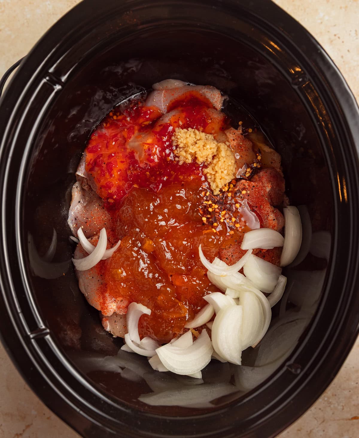 Slow cooker with apricot preserves, onion and seasoning over chicken.