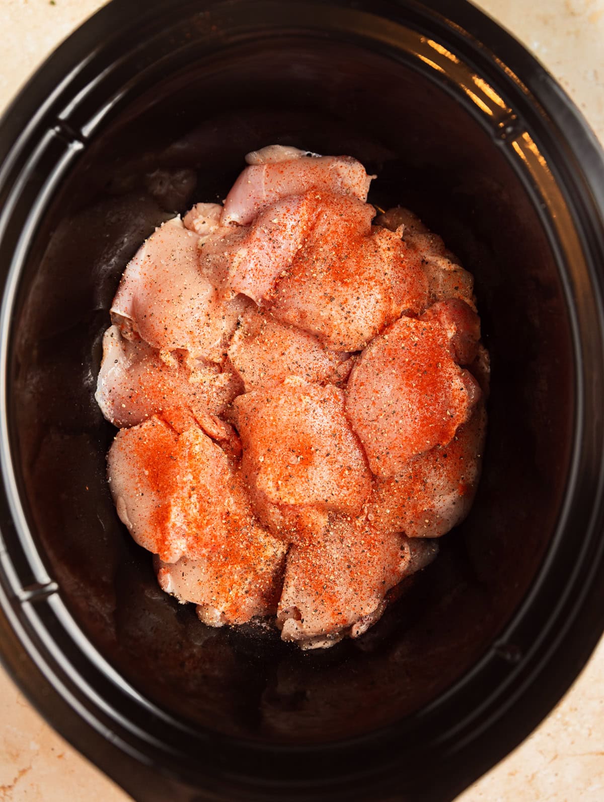 Chicken thighs in crockpot with seasoning on top.