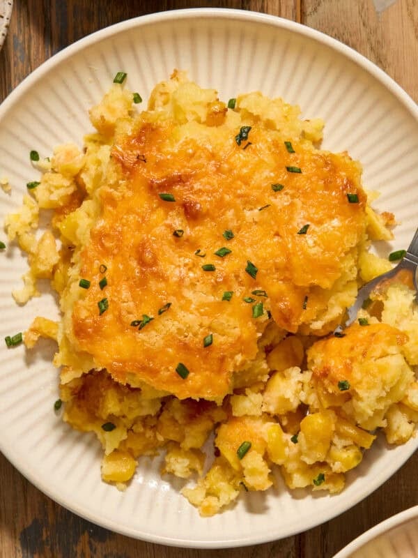 Cheesy cornbread casserole on white dish with fork scooping in.