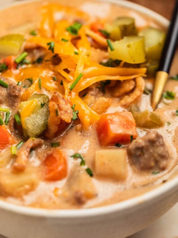 Crockpot cheeseburger soup served in bowl topped with cheese, pickles and parsley.