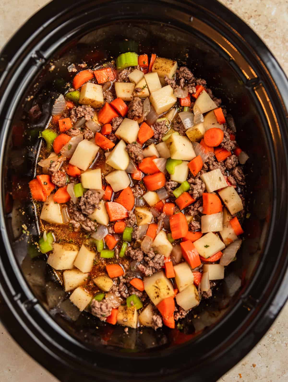 Meat, vegetables and broth in slow cooker.