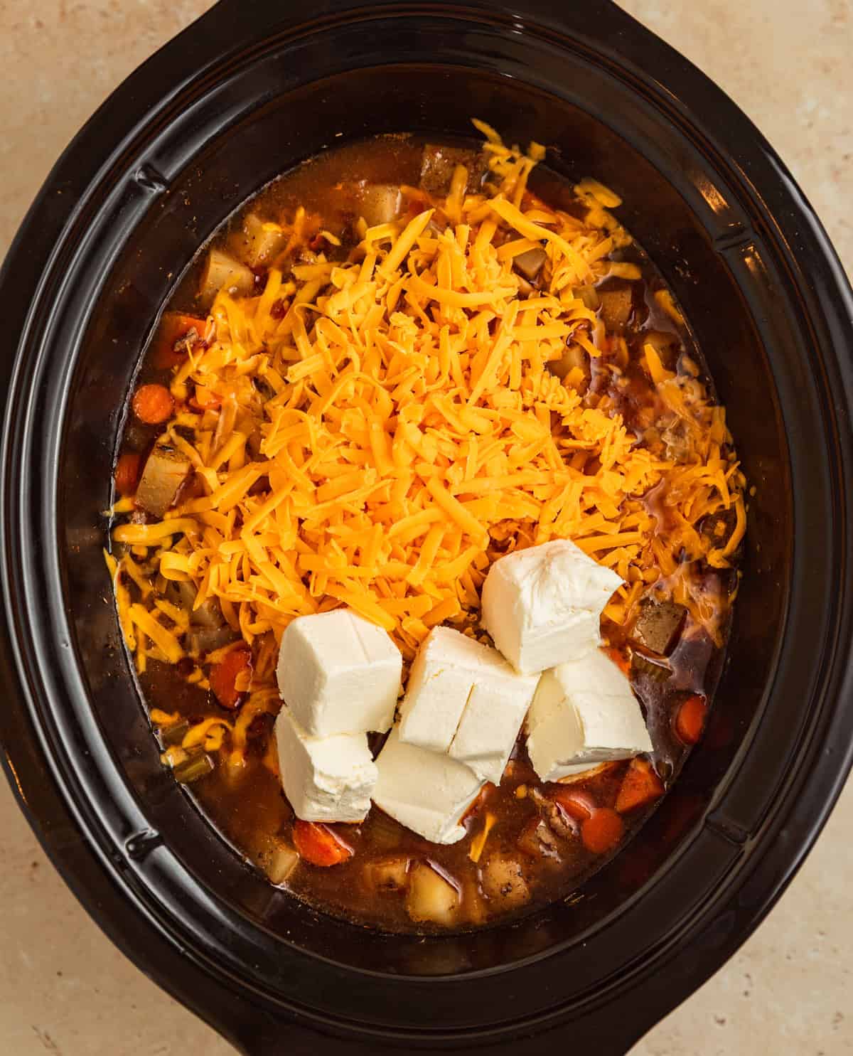 Shredded cheddar cheese and cubed cream cheese added to crockpot soup.