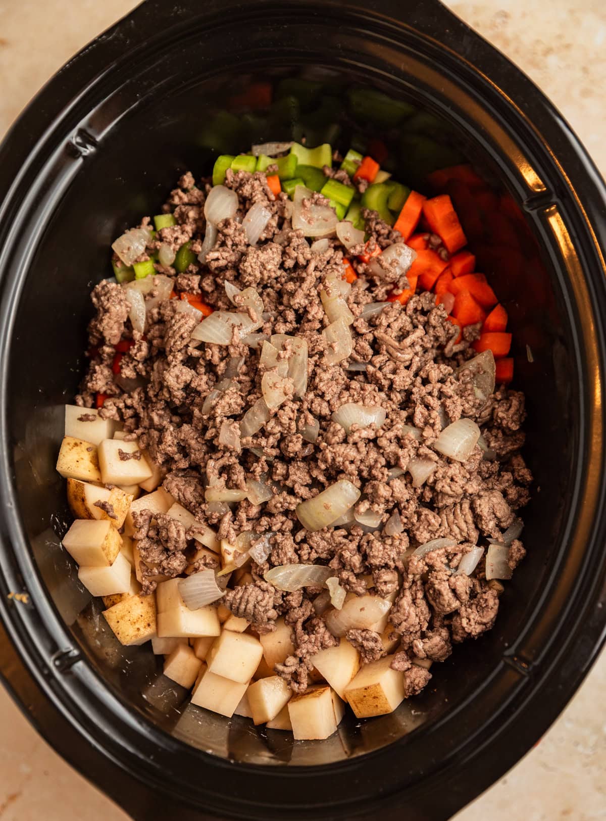 Beef, potatoes, carrots, and celery in crockpot before cooking.