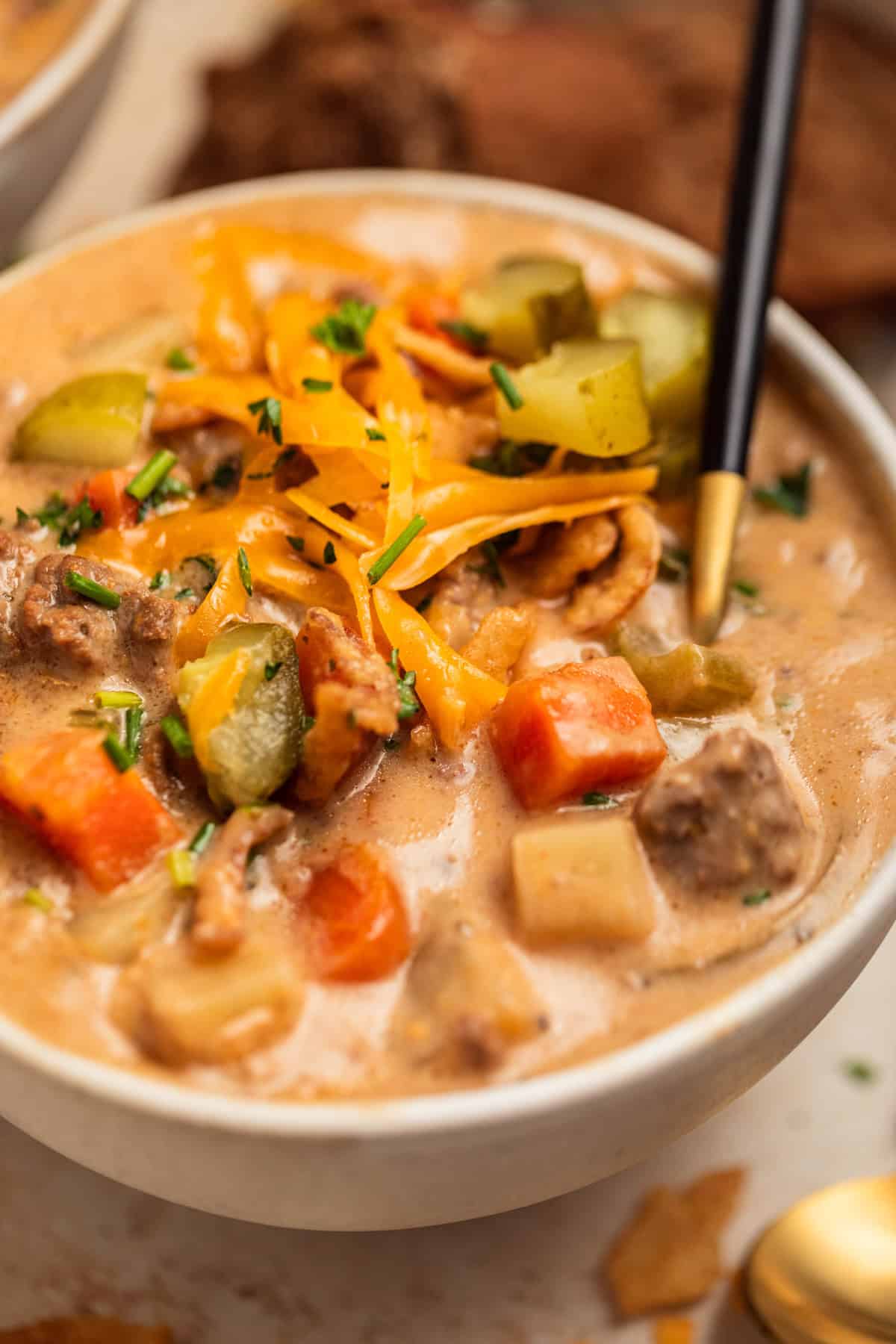 Cheeseburger soup in bowl with cheese and pickles on top and spoon scooping in.