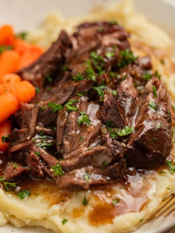 Short ribs with gravy over top on plate with potatoes and carrots.