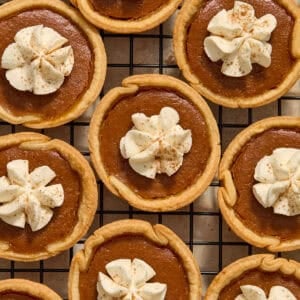 Mini pumpkin pies on cooling rack with whipped cream piped on top.