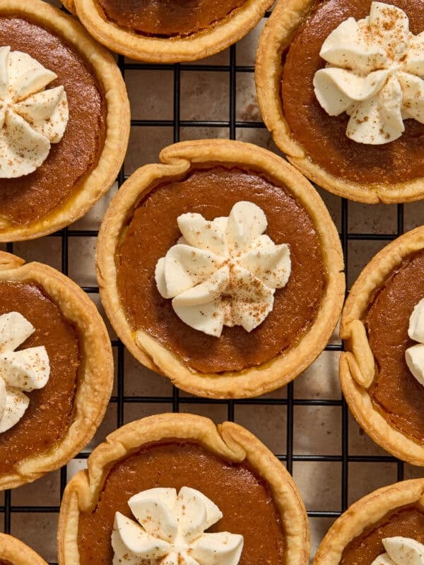 Mini pumpkin pies on cooling rack with whipped cream piped on top.