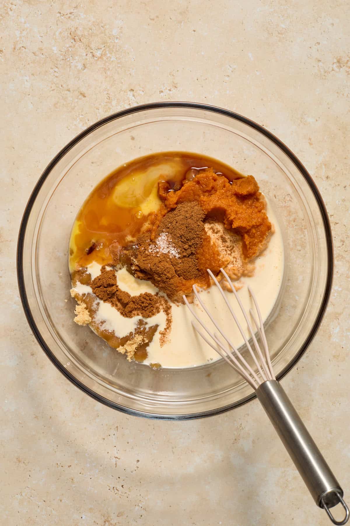 Pumpkin, evaporated milk, butter and other ingredients in bowl with whisk.