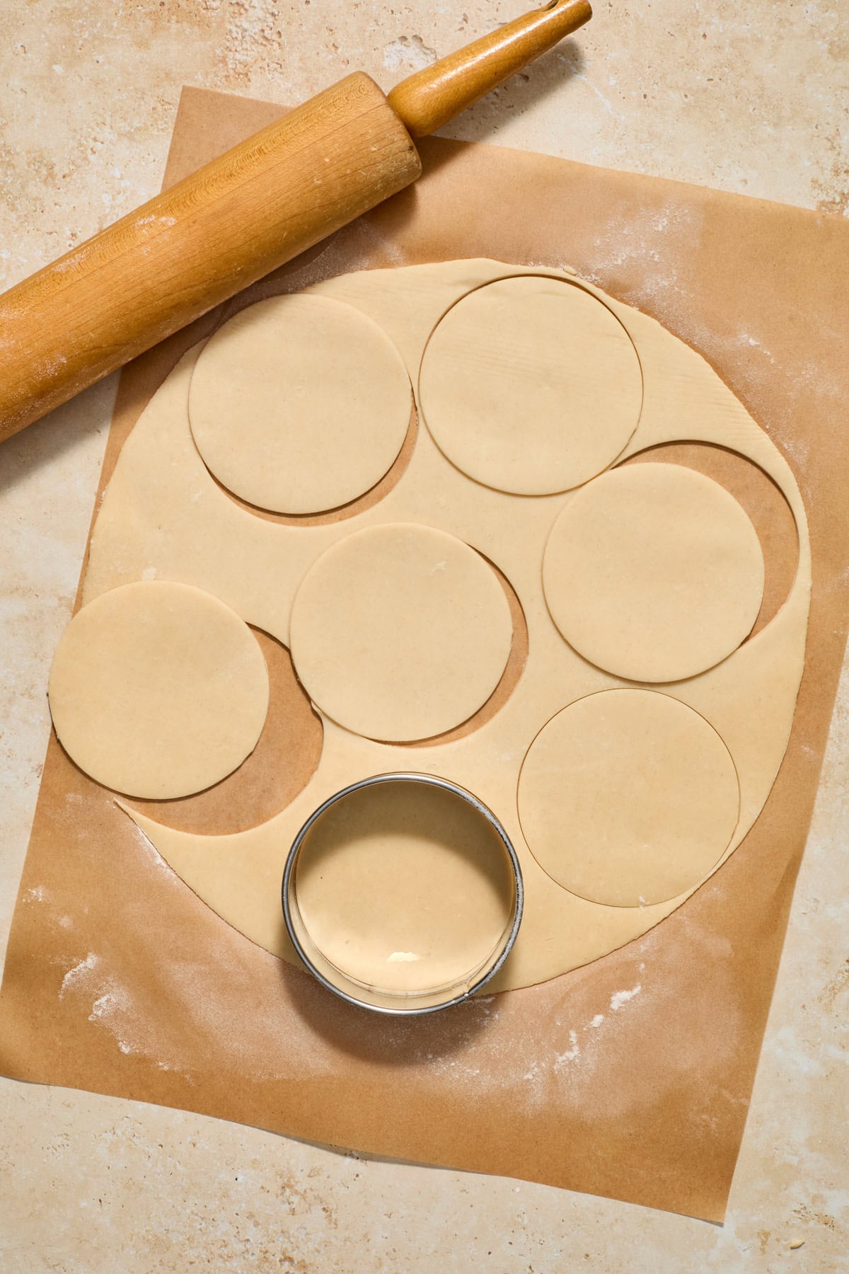 Pie crust rolled on parchment paper with rolling pin and biscuit cutter.