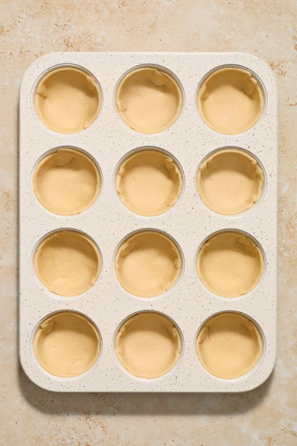 Muffin tin with pie crust in each muffin cavity.