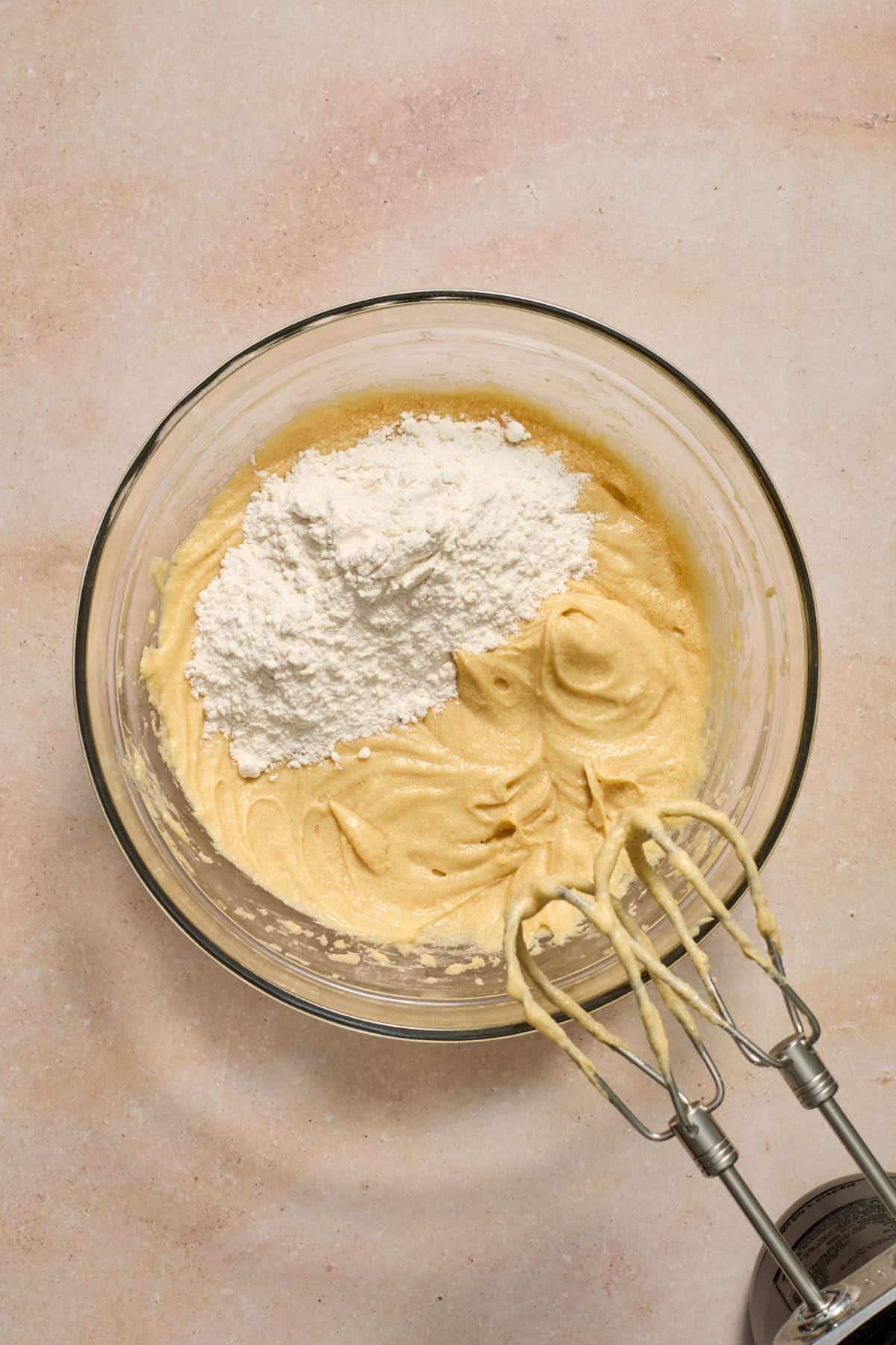 Dry ingredients added to wet ingredients in bowl with hand mixer propped beside bowl.