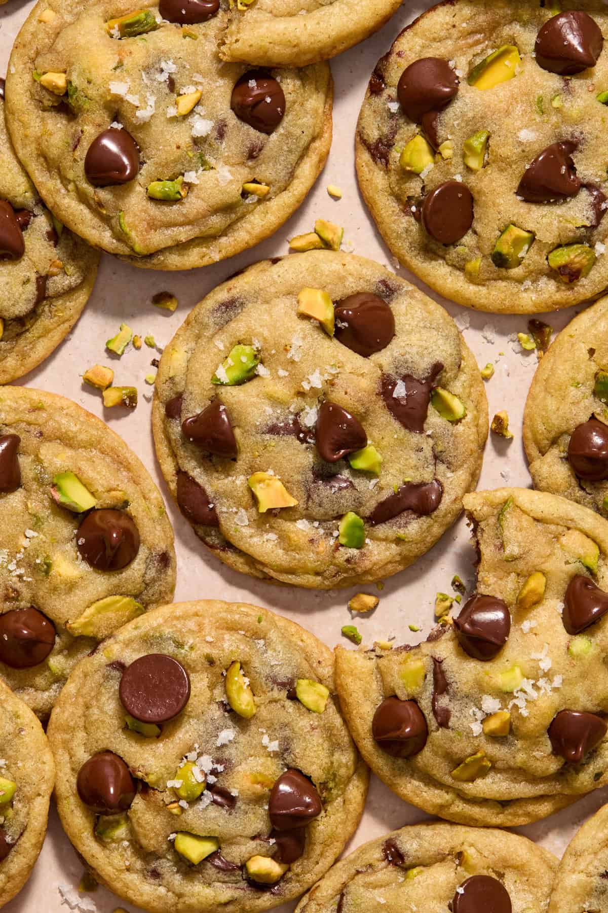 Sea salt pistachio chocolate chip cookies arranged on surface with flaked sea salt over top.