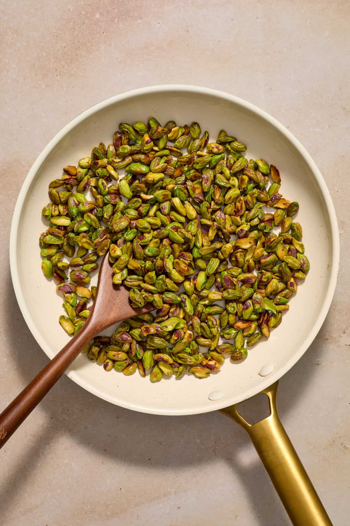 Pistachios in skillet with wooden spoon.