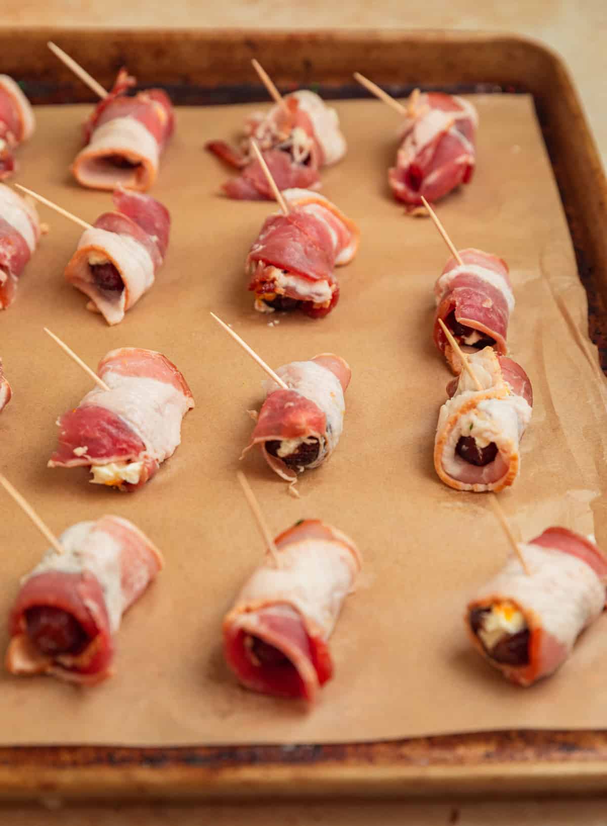Bacon wrapped dates on baking sheet.