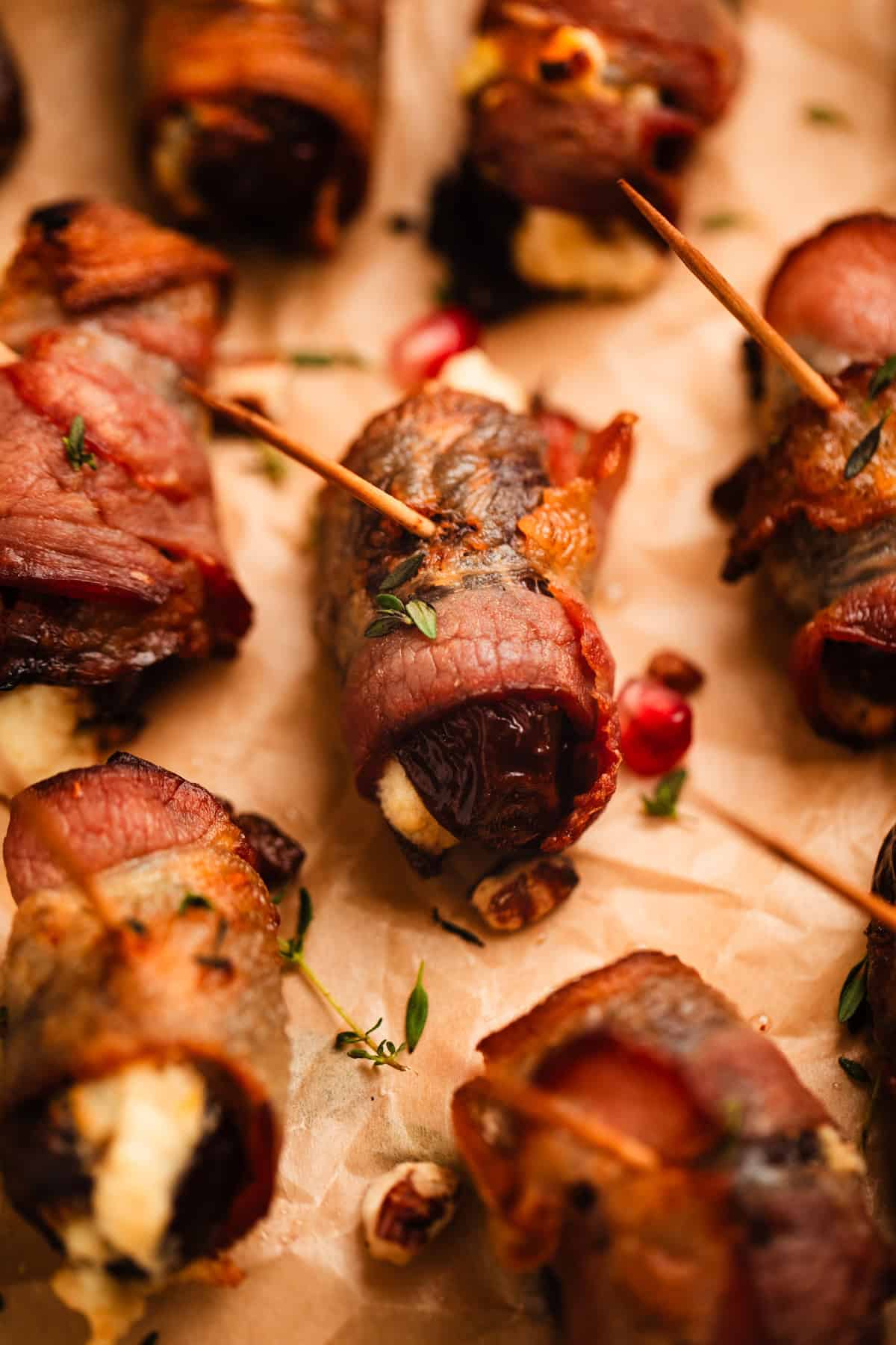 Stuffed dates on wrapped in bacon on parchment paper.
