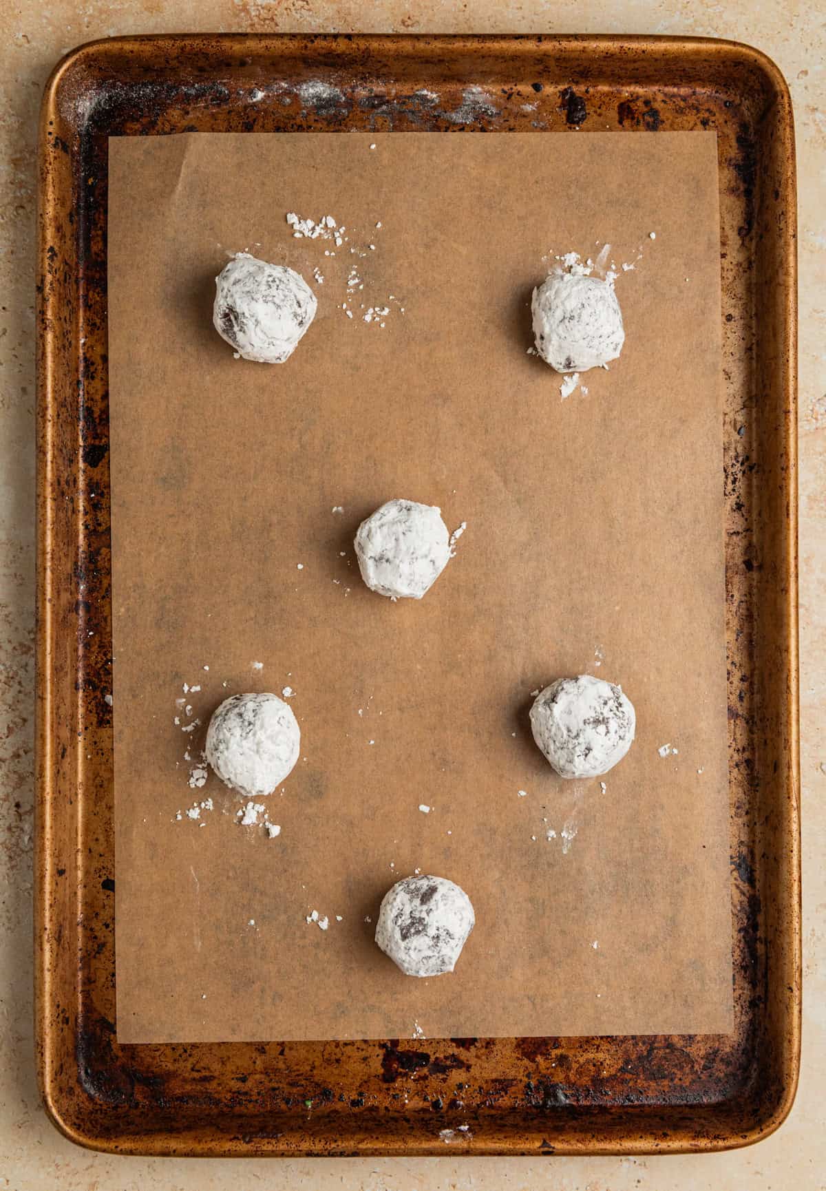 Powdered sugar covered chocolate cookie dough balls on parchment lined pan.