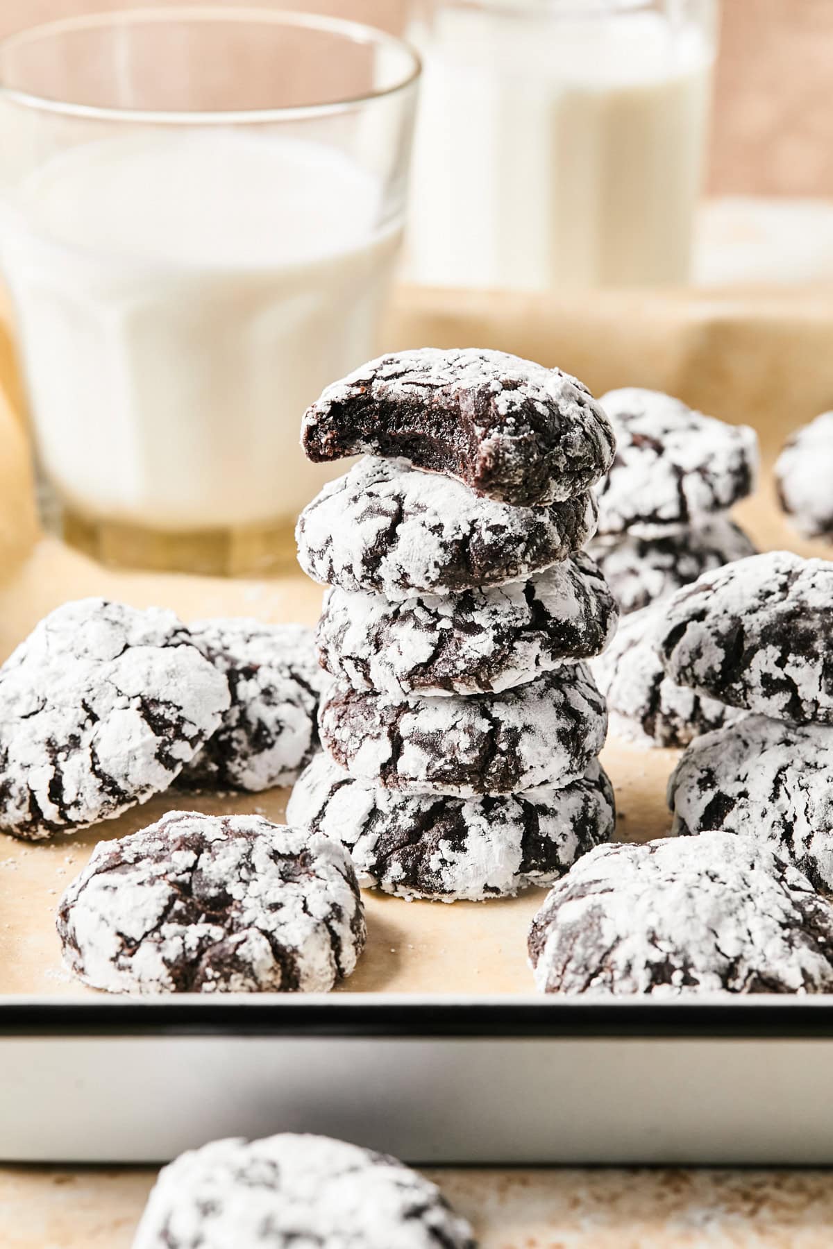 Stack of chocolate crinkle cookies on parchment with milk.